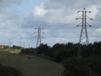 High-voltage electrical transmission towers and power lines stretching across a rural landscape with green fields and trees